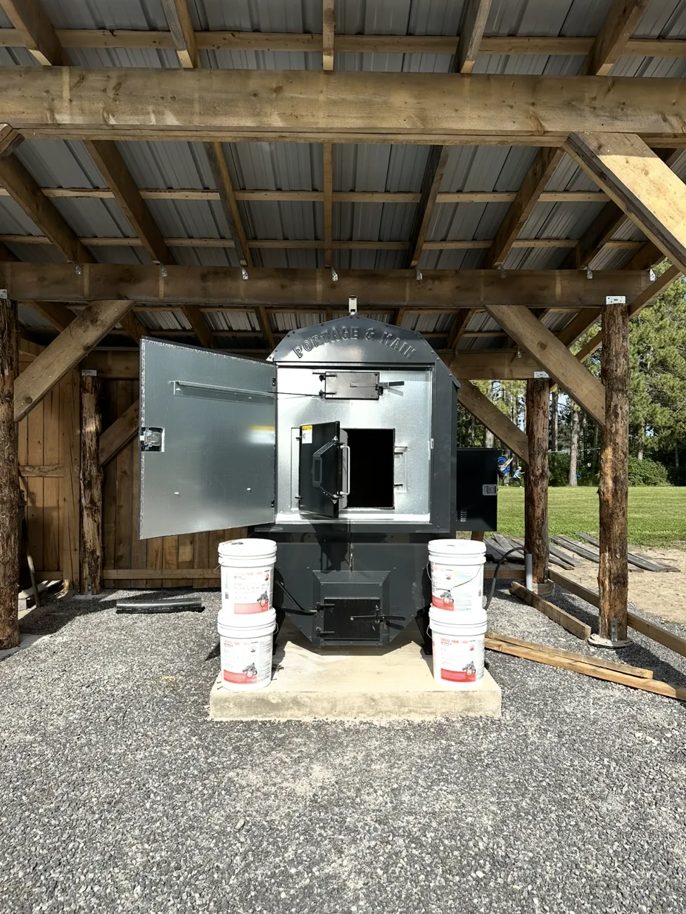 Front view of a Portage & Main outdoor boiler under a timber-frame shelter with its doors open