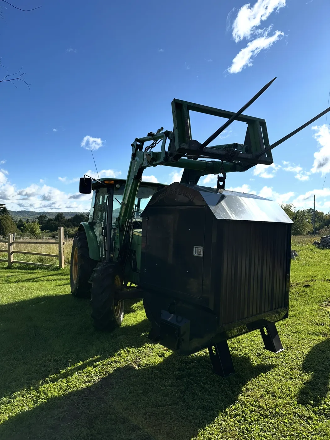 A tractor lifting a Portage & Main outdoor boiler into place on a farm